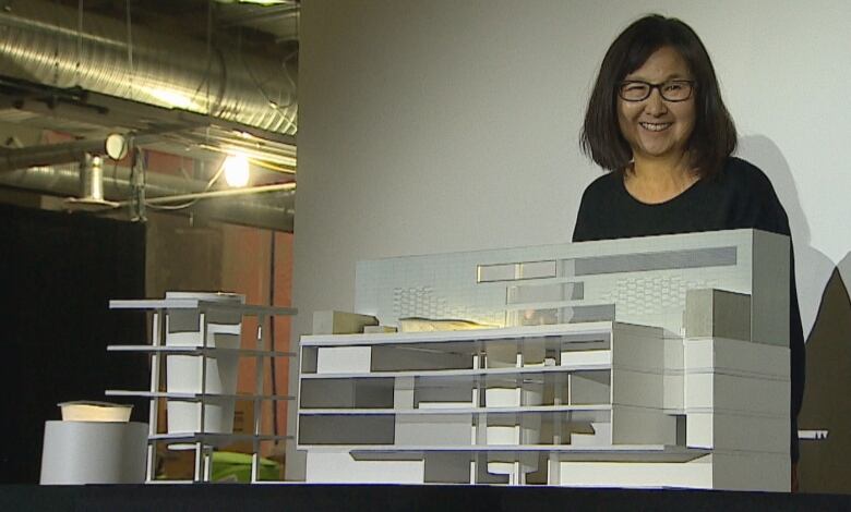 A woman of Asian descent stands behind an architectural model.