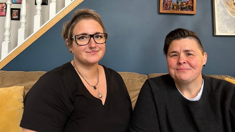 Two women clad in black tees sit next to each other.