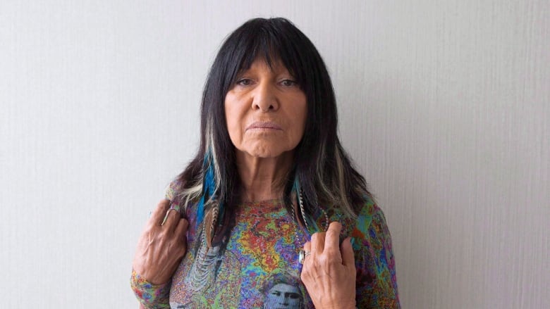 A portrait of a woman wearing a colourful shirt in front of a gray wall.