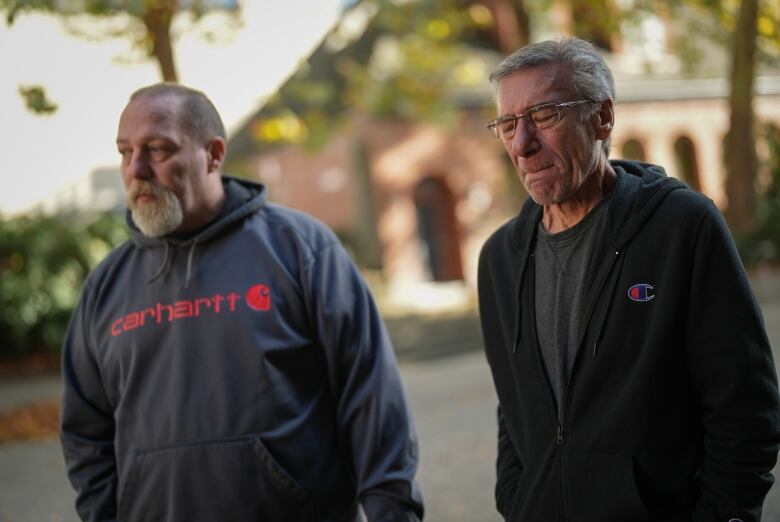 Aron and Darrel Crimeni, two casually dressed white men, hold back tears as they stand side by side.