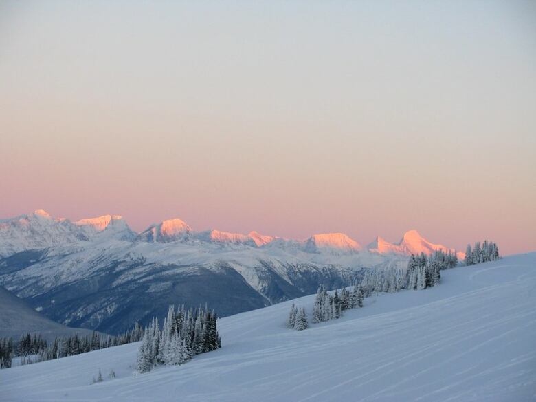 A snow capped mountain at sunset. The mountain has a blue hue and the sky indicates sunset with a faint glow of pink in the air.