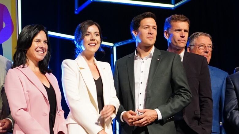 Group of men and women in suits line up for a photo on a stage.