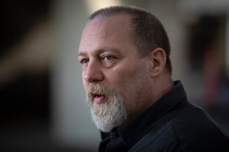 Aron Crimeni, a middle-aged white man with a grey beard, is pictured in a profile headshot.