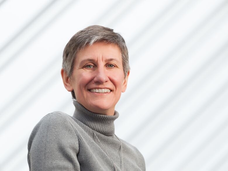 A woman with short, grey hair wearing a grey turtleneck smiles for a portrait photo.