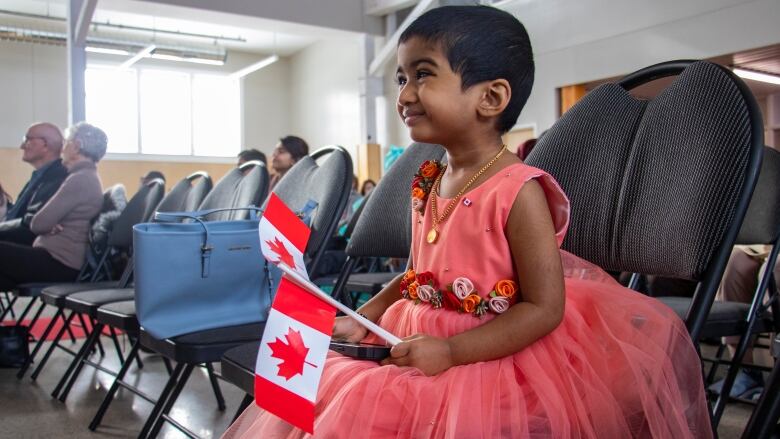 A little girl in a fancy dress holds Canadian flags.