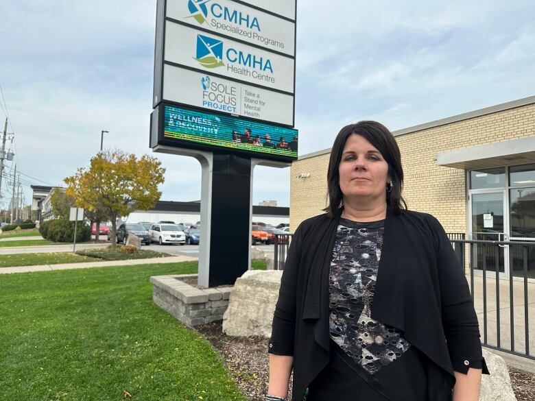 A woman stands outside of a building and behind her is the sign for the organization.