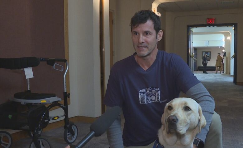 a man in a blue shirt talks into a microphone while sitting on the ground with a dog