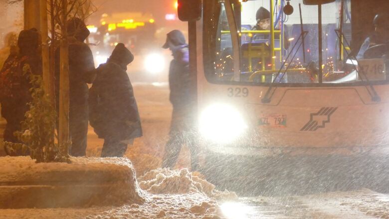 People get onto a bus on a snowy, dark morning