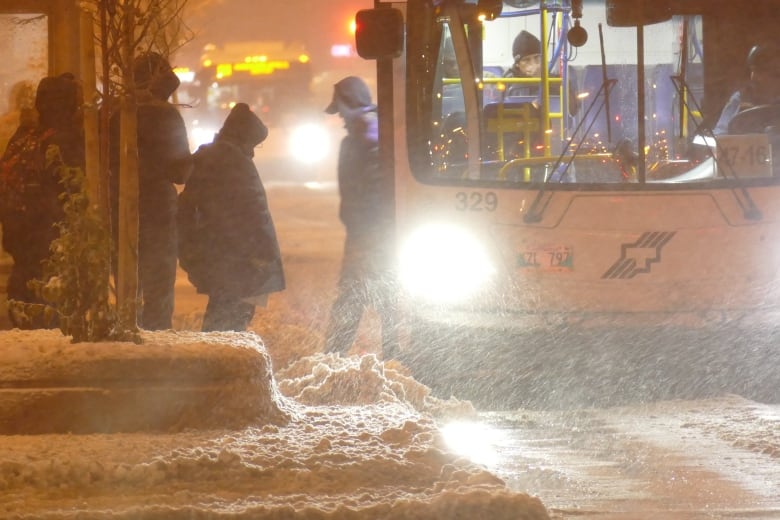 People get onto a bus on a snowy, dark morning