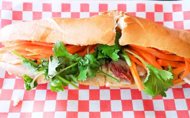 Vietnamese banh mi sits on top of a red and white checkered parchment paper.