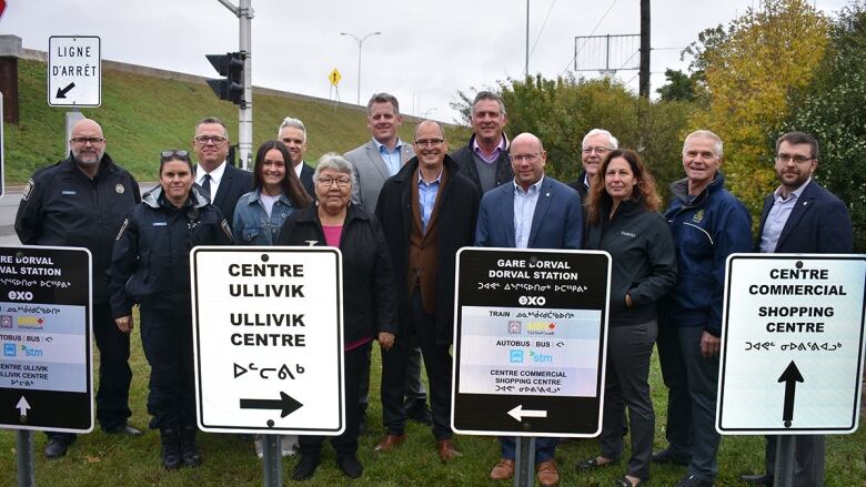 A group of people stand behind road signs written in three different languages.