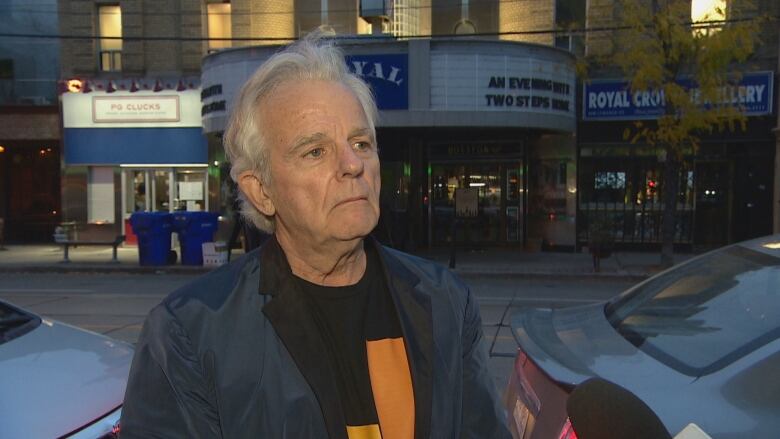 Picture of a man standing on the street outside a theatre where a find raiser his being held for a proposal to build cabins for people living in tents or shelters.