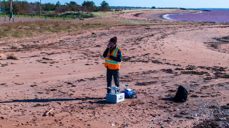 A man in a safety vest talks on a walkie-talkie with his drone ready to launch 