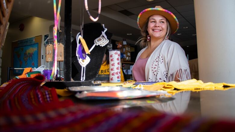 A woman sits smiling in a beaded hat at a table full of beaded earings.