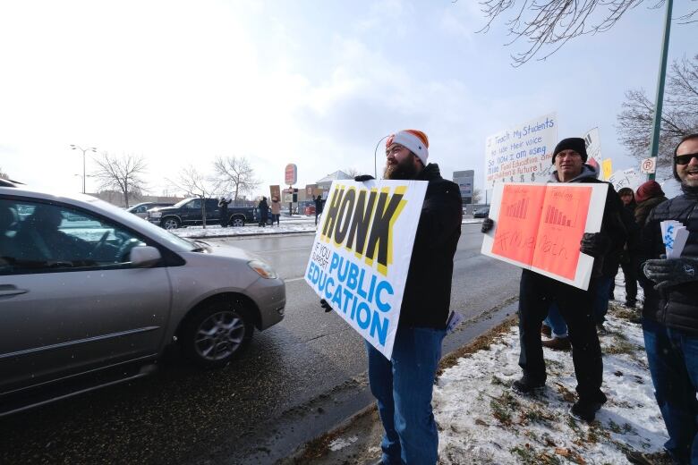 Curtis Bourassa holds a sign asking drivers to honk in support, while wearing winter clothing