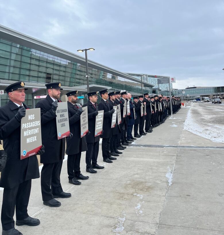 Pilots are seen in uniform standing next to each other and holding up placards.