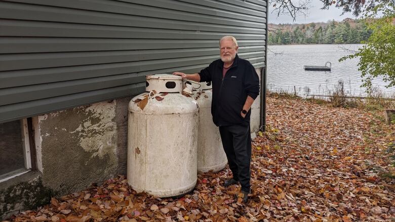 A man stands next to a propane tank outside of his home.