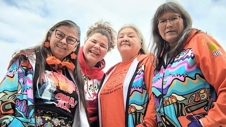 Four women are pictured smiling toward the camera.