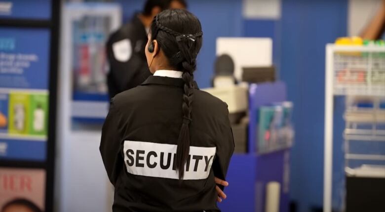 A security personnel with a vest that reads 'Security' has her back turned to the camera