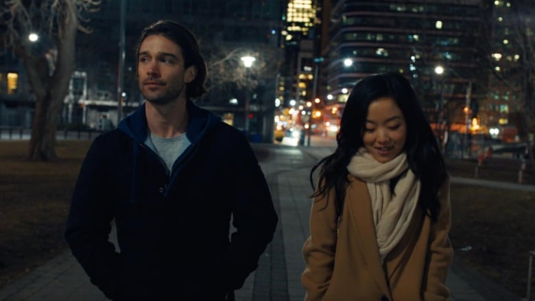 Joe Scarpellino (left) and Andrea Bang (right) in Stay the Night. They're bundled up for cold weather, walking in a city at night. 