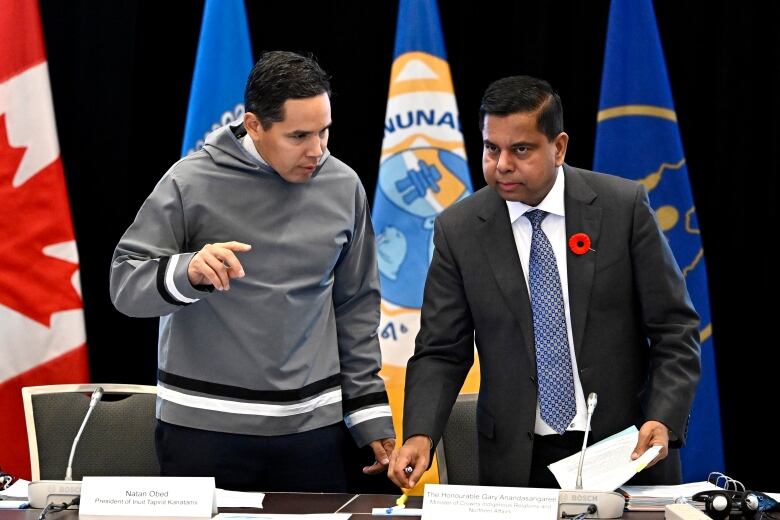 Two politicians sit down for a committee meeting in a room.