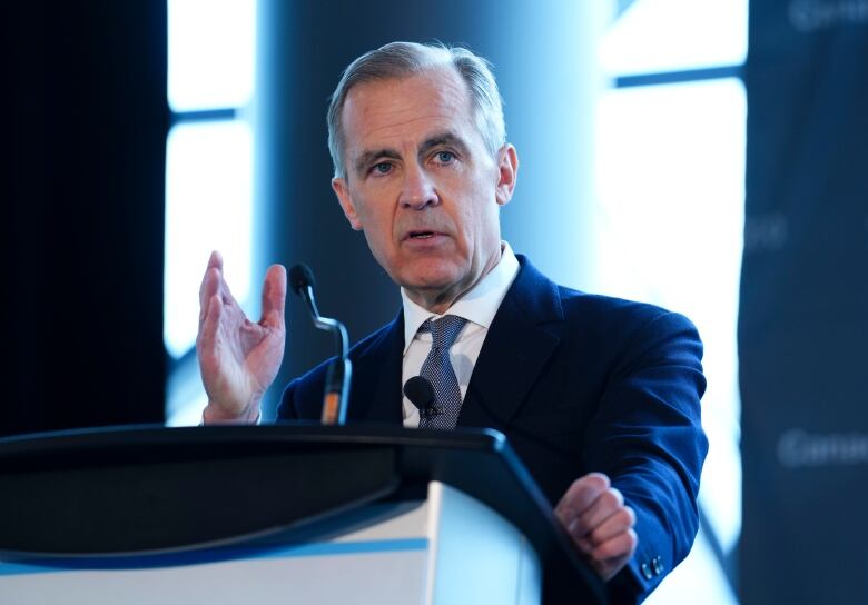 A man in a suit and tie gestures with his hand as he speaks at a podium.