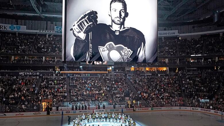 With a picture of a late hockey player shown on an arena videoboard, NHL players gather at centre ice below in tribute.