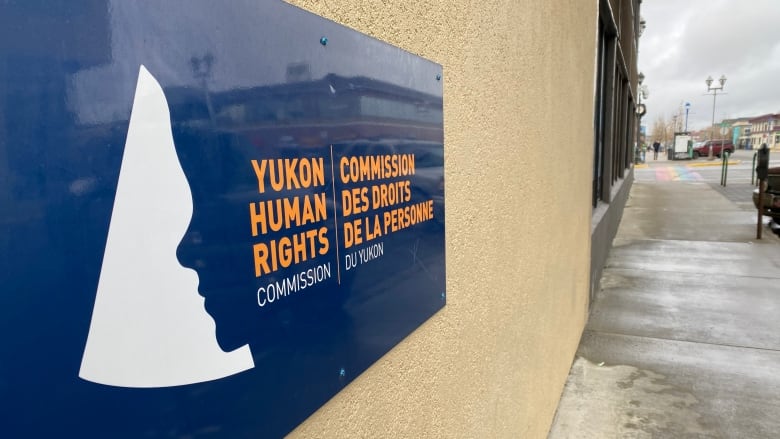 A sign on a wall alongside a sidewalk reads, 'Yukon Human Rights Commission.'