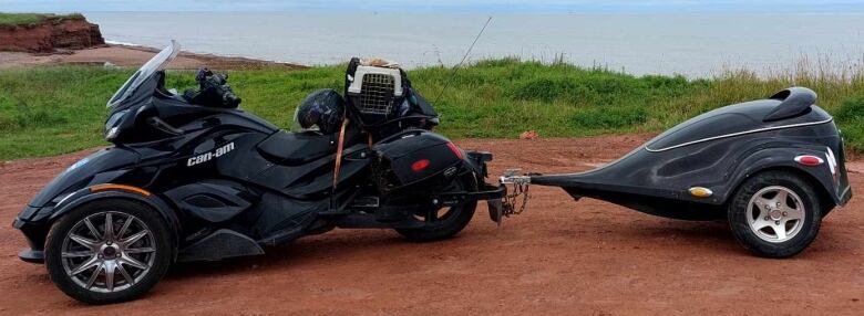 A black, three-wheeled bike is loaded up, with dog carrier on the back, and a trailer for supplies. 