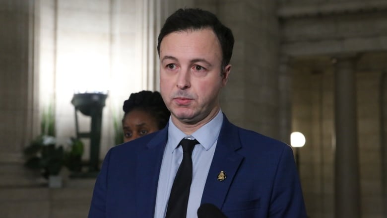 A man in a blue suit stands in a darkened hallway of a legislative building.