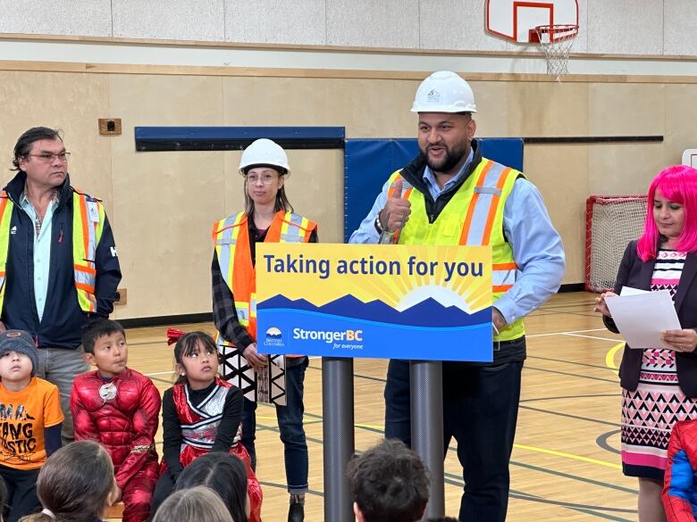 A man wearing a construction outfit stands at a podium labelled 