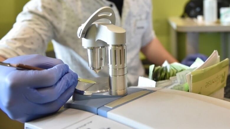 A person in blue rubber gloves places a substance on a plate underneath a steel testing device.