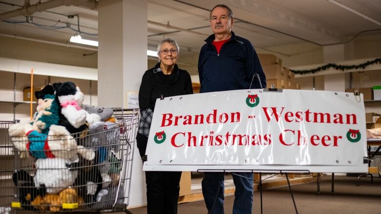 A man and woman stand in front of a story that says Brandon-Westman Christmas Cheer.