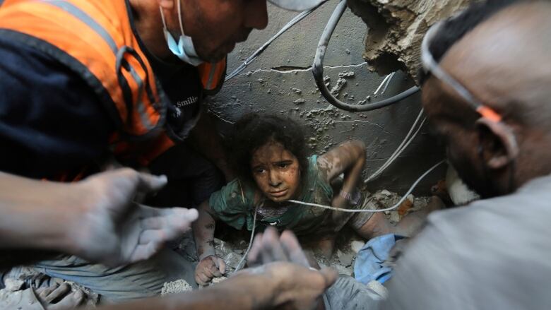 Three men try to pull a young Palestinian girl out from beneath a slab of concrete and other debris. 