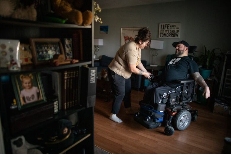 A man in a wheelchair smiles as a woman adjusts a setting on his wheelchair.