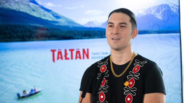 A man poses in front of a TV that reads 'Tahltan'.