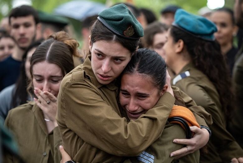 Two young women in military uniforms cry and embrace.