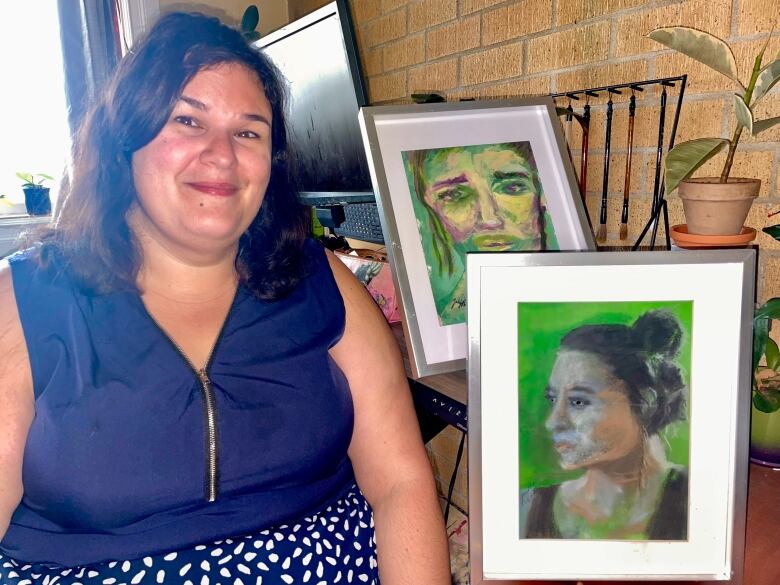 A woman sits beside two framed paintings.