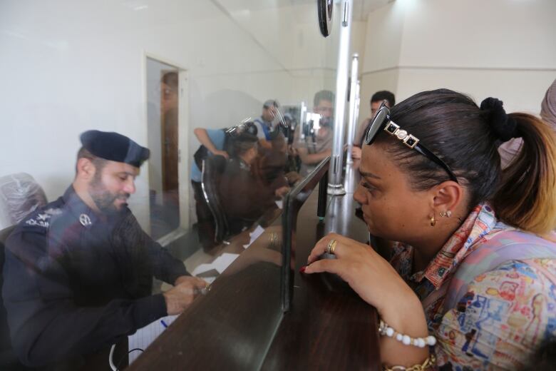 A woman on the right waits for an official to look over her travel documents at a border crossing.