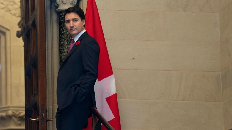 A man in a suit stands next to a Canadian flag.