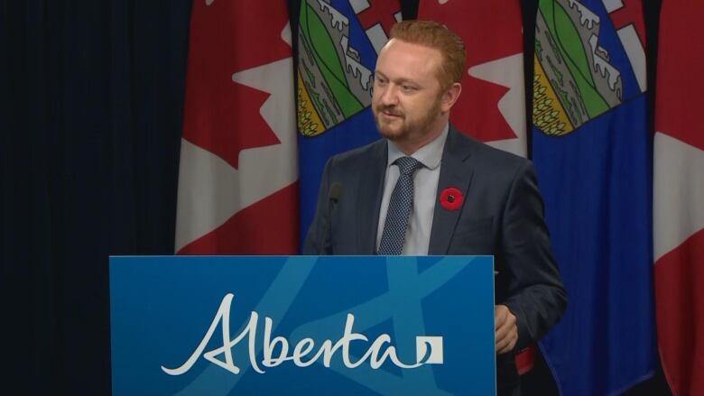 A man stands behind a podium with 'Alberta' written across the front.