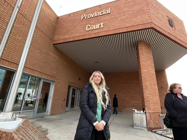 Caitlin Erickson is standing with the brick exterior of the provincial court behind her