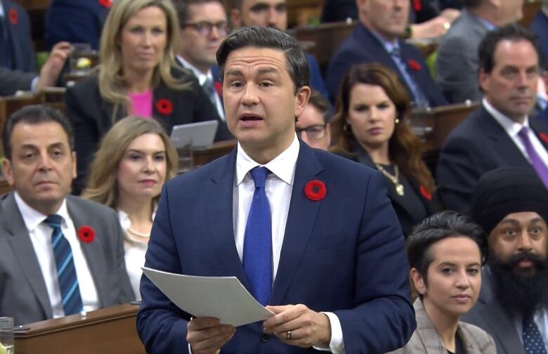 Pierre Poilievre in the House of Commons, holding a paper, wearing a poppy.