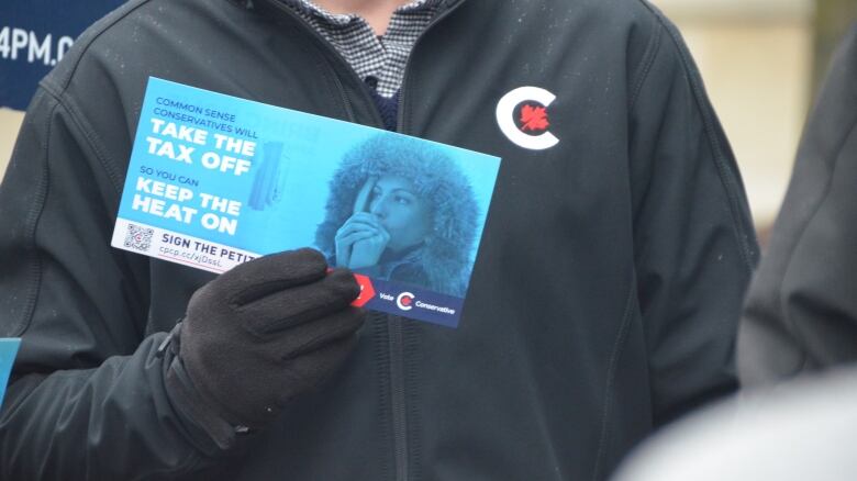 A person wearing a sweater with a Conservative party logo holds a flyer