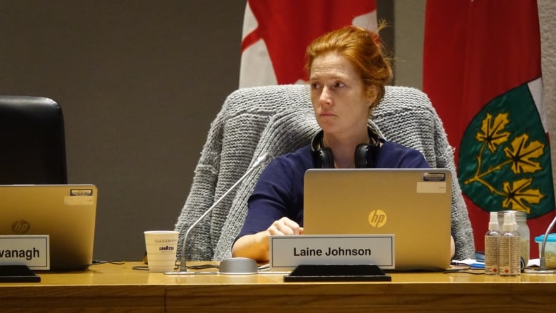 red-haired woman in a blue dress looks off to the side