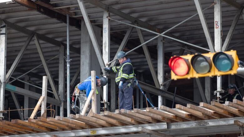 Workers in high-visibility vests and other protective equipment work on a multi-story building. The interior frame of the building is exposed.