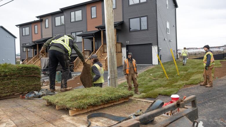 Workers in high visibility vests are seen in a line passing sod to each other to lay down in the yard of a home.