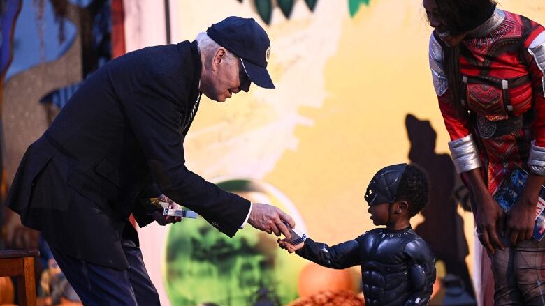 Elderly man hands candy to a child dressed up on Halloween.