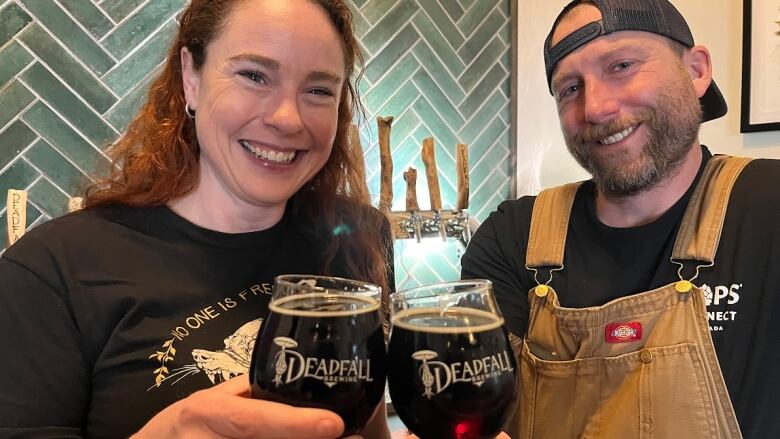 A woman and man clink glasses of beer while smiling at the camera.