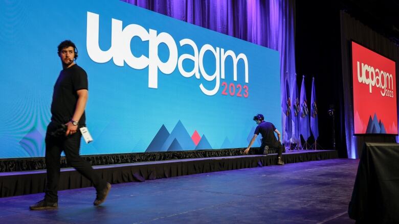 Two stagehands set up a sign on a convention stage.